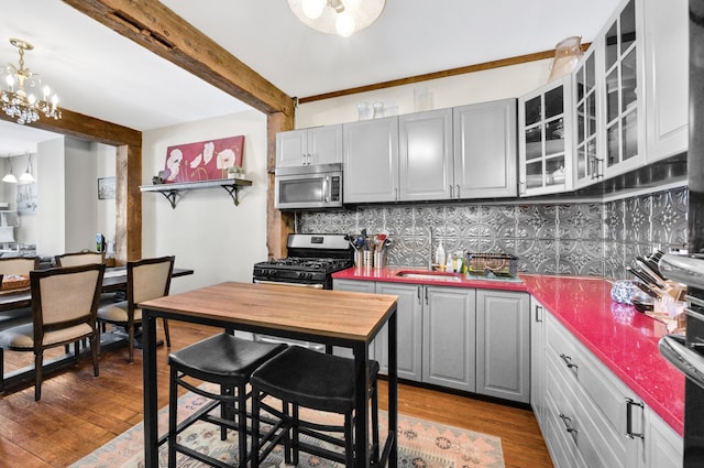 kitchen with appliances with stainless steel finishes, gray cabinetry, a sink, and beamed ceiling