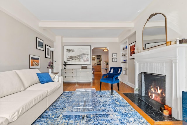 living room with wood finished floors, a fireplace, beamed ceiling, built in shelves, and arched walkways