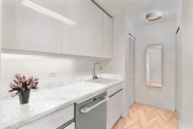 kitchen featuring a sink, stainless steel dishwasher, white cabinetry, and baseboards
