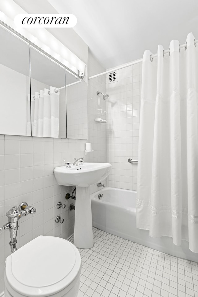 bathroom with tile patterned flooring, shower / bath combo with shower curtain, toilet, and tile walls