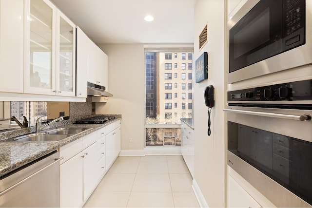 kitchen with a sink, baseboards, white cabinets, under cabinet range hood, and stainless steel appliances