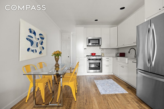 kitchen with appliances with stainless steel finishes, a sink, light wood-type flooring, tasteful backsplash, and ornamental molding