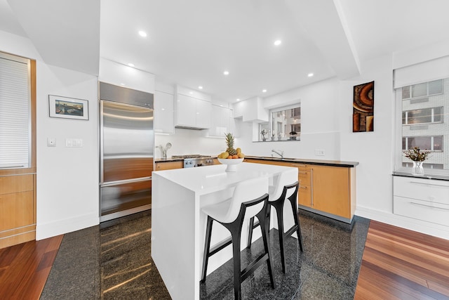 kitchen featuring stainless steel built in refrigerator, a sink, a breakfast bar area, baseboards, and modern cabinets