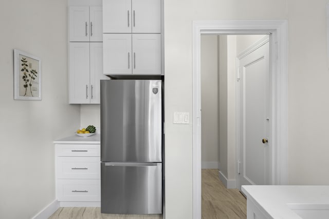 kitchen featuring baseboards, white cabinetry, light countertops, and freestanding refrigerator