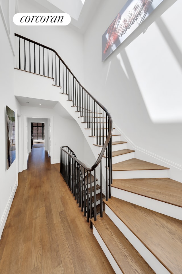 stairway featuring baseboards, wood finished floors, and a high ceiling