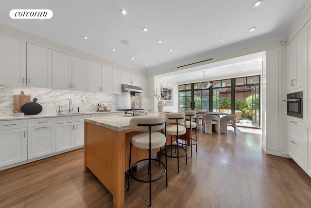 kitchen with a sink, white cabinetry, backsplash, and under cabinet range hood