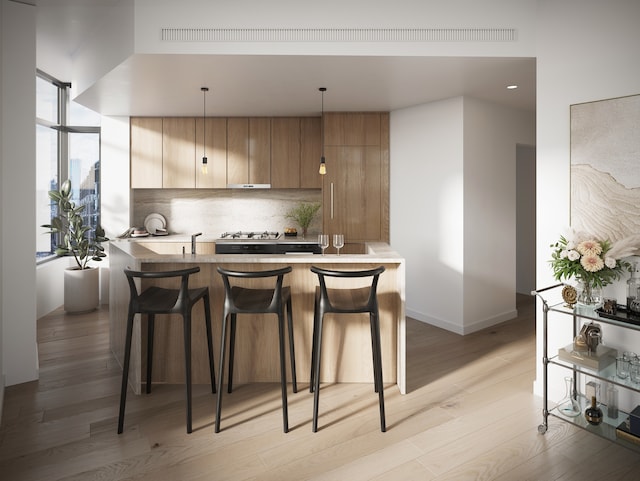 kitchen featuring a breakfast bar, tasteful backsplash, light wood-style floors, modern cabinets, and brown cabinets