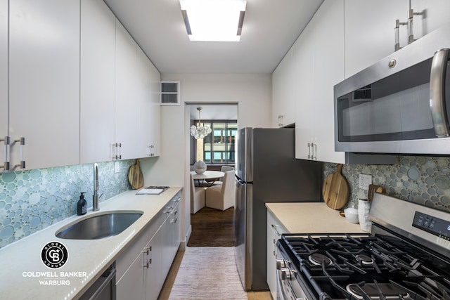 kitchen with appliances with stainless steel finishes, a sink, light wood-type flooring, light countertops, and white cabinets