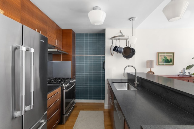 225 W 60th St Unit 14F, New York City, NY 10023 - kitchen featuring appliances with stainless steel finishes, a sink, under cabinet range hood, dark countertops, and wood finished floors
