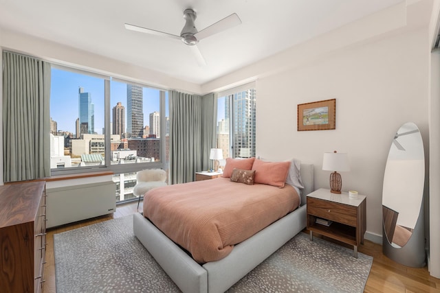 225 W 60th St Unit 14F, New York City, NY 10023 - bedroom with a view of skyline, wood finished floors, ceiling fan, and baseboards