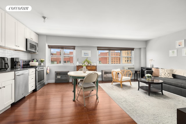 living room with dark wood-style floors, radiator heating unit, baseboards, and a wall mounted air conditioner