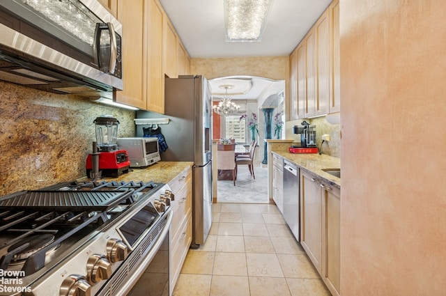 kitchen with appliances with stainless steel finishes, arched walkways, a chandelier, light tile patterned floors, and backsplash