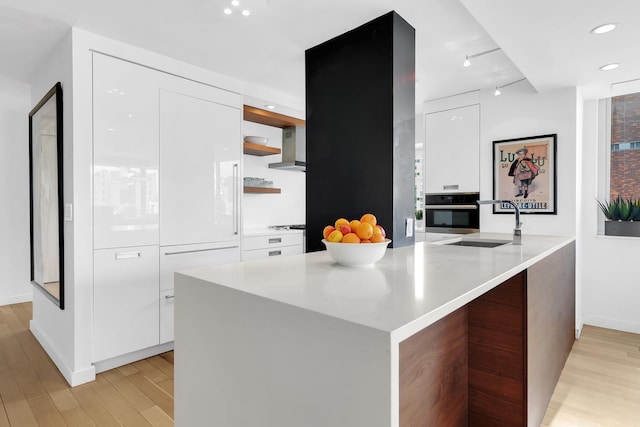 kitchen with white cabinets, oven, a sink, light wood-type flooring, and modern cabinets