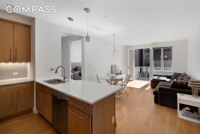 kitchen with light wood finished floors, a sink, a peninsula, dishwasher, and open floor plan