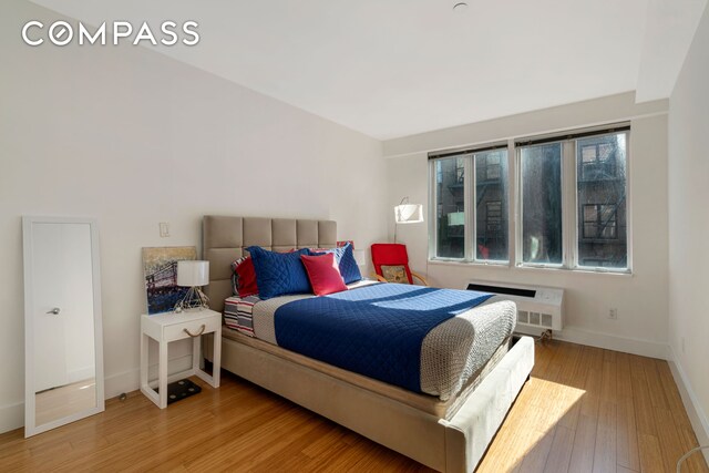 bedroom with baseboards, a wall mounted air conditioner, and wood finished floors