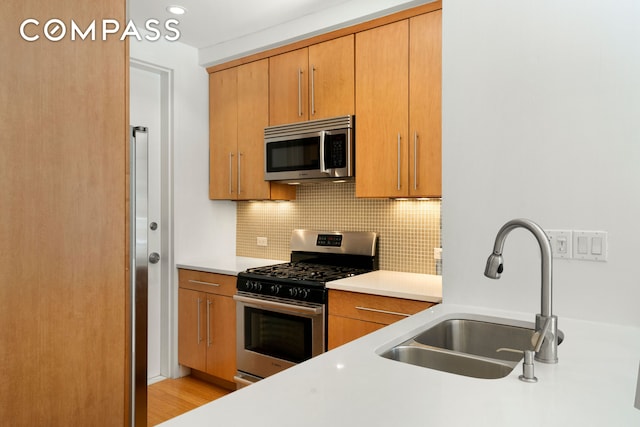 kitchen with tasteful backsplash, appliances with stainless steel finishes, light countertops, brown cabinets, and a sink