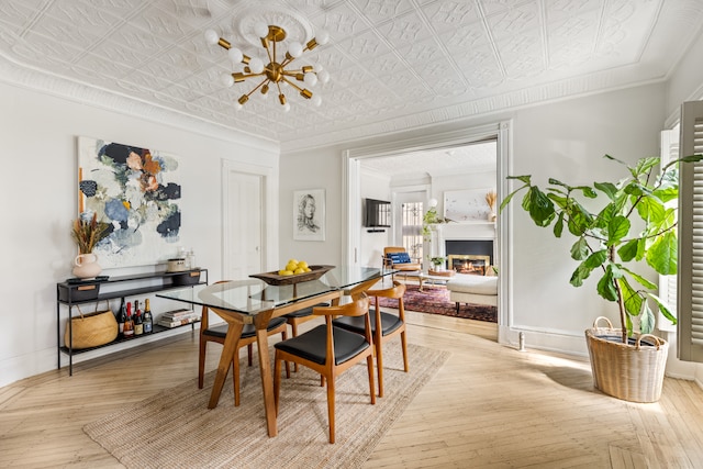 dining area with an ornate ceiling, light wood-type flooring, baseboards, crown molding, and a warm lit fireplace
