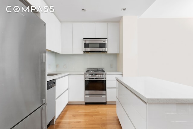 148 E 24th St Unit 12B, New York City, NY 10010 - kitchen with appliances with stainless steel finishes, light countertops, white cabinets, light wood-style flooring, and recessed lighting
