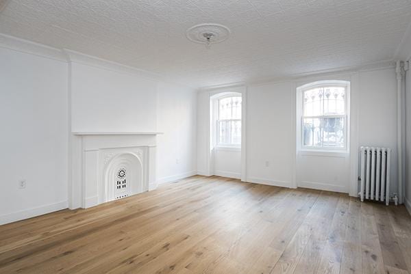 unfurnished living room featuring baseboards, radiator, and hardwood / wood-style floors