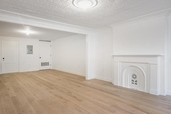 unfurnished living room with light wood-style floors, baseboards, and electric panel