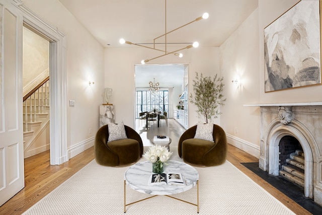 living area with stairs, wood finished floors, baseboards, a chandelier, and a fireplace with flush hearth