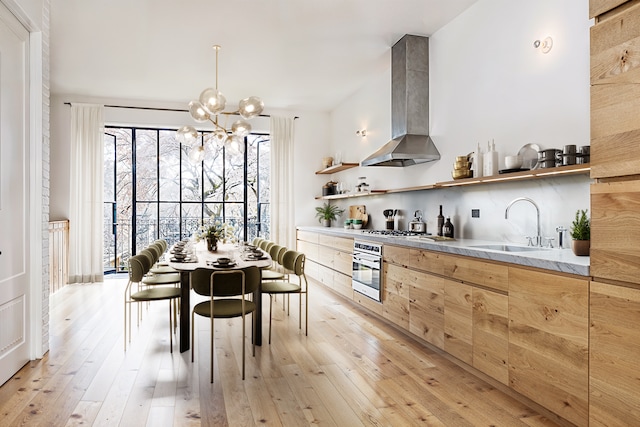 kitchen with wall chimney range hood, appliances with stainless steel finishes, modern cabinets, open shelves, and a sink