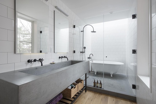 full bath with a sink, tile walls, wood finished floors, backsplash, and a soaking tub
