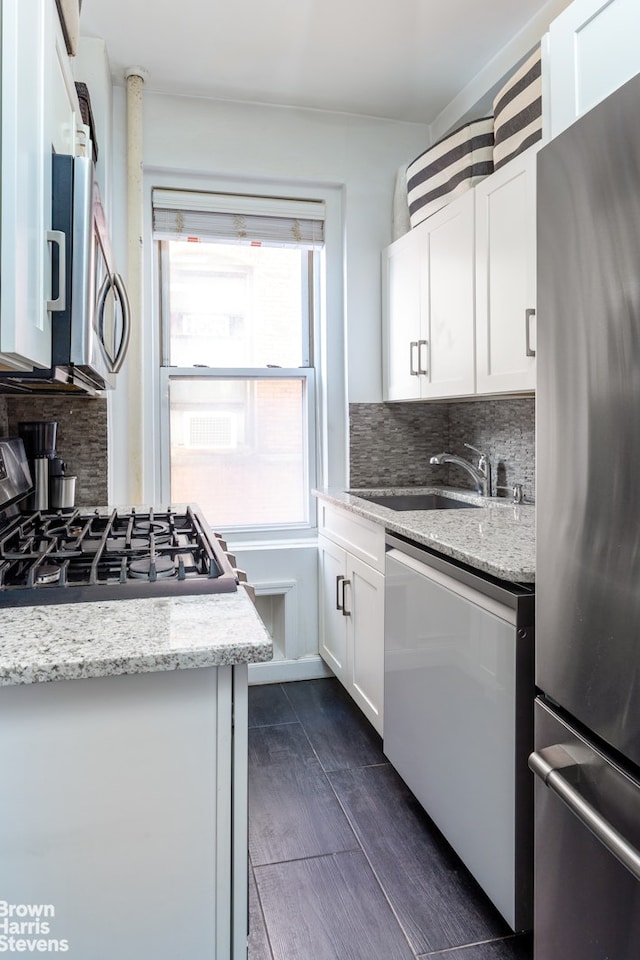 kitchen featuring appliances with stainless steel finishes, a sink, decorative backsplash, white cabinetry, and light stone countertops