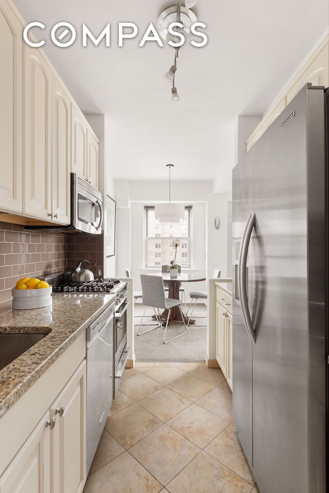 11 5th Ave Unit 18A, New York City, NY 10003 - kitchen featuring appliances with stainless steel finishes, cream cabinetry, decorative backsplash, light tile patterned floors, and light stone countertops