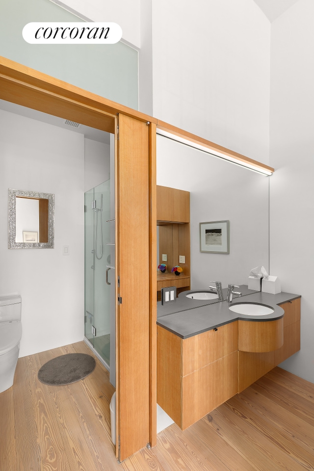 full bathroom featuring toilet, wood finished floors, a shower stall, and double vanity