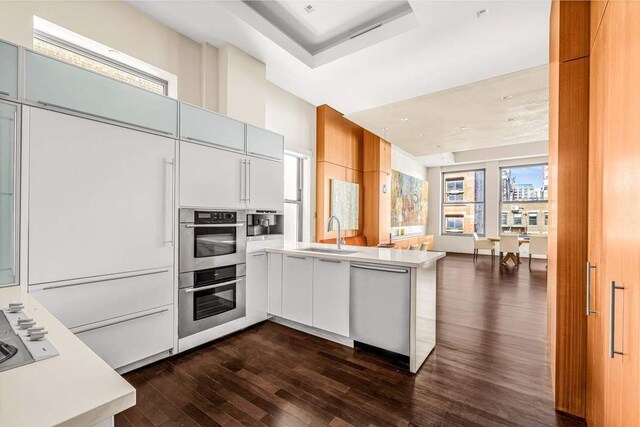 92 Greene St Unit 4, New York City, NY 10012 - kitchen featuring dark wood-style flooring, appliances with stainless steel finishes, a sink, light countertops, and a peninsula