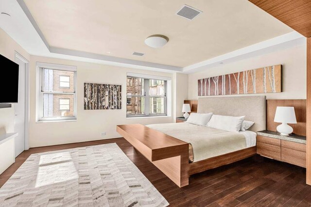 bedroom featuring dark wood-style floors, visible vents, and a tray ceiling