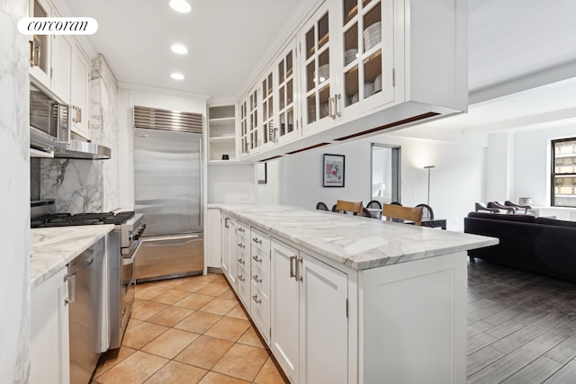 12 W 72nd St Unit 12D, New York City, NY 10023 - kitchen with appliances with stainless steel finishes, a peninsula, white cabinets, decorative backsplash, and recessed lighting