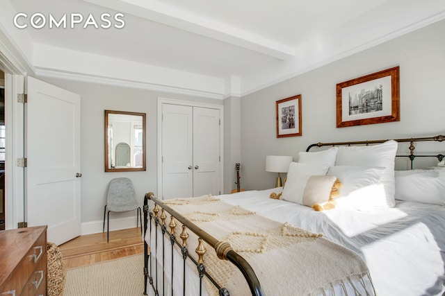 bedroom with light wood-style flooring, a closet, beamed ceiling, and baseboards