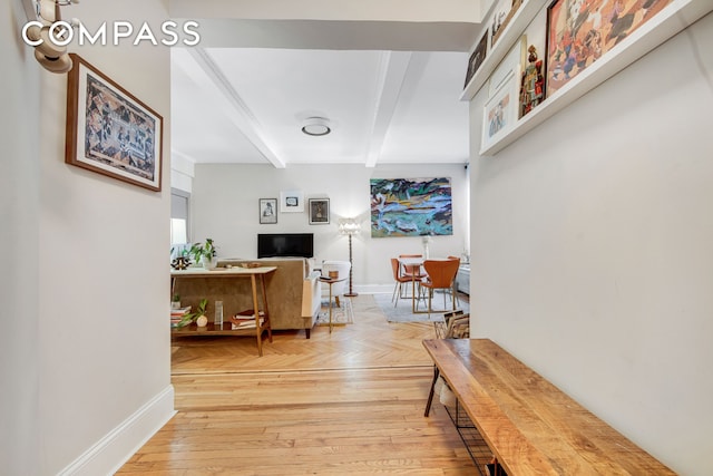 corridor with beamed ceiling, light wood-style flooring, and baseboards