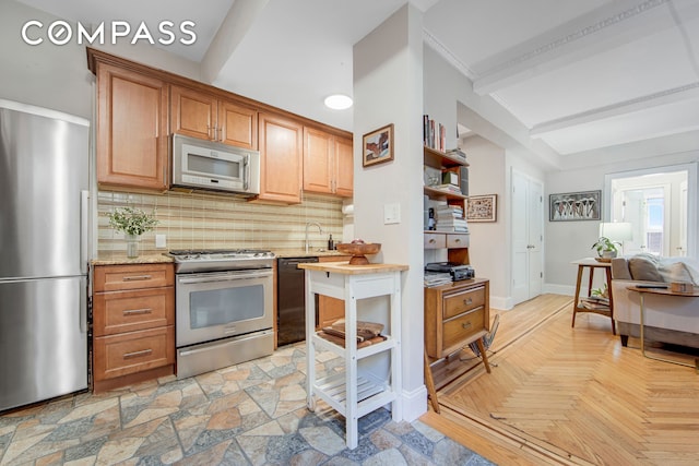 kitchen with appliances with stainless steel finishes, tasteful backsplash, a sink, baseboards, and light stone counters
