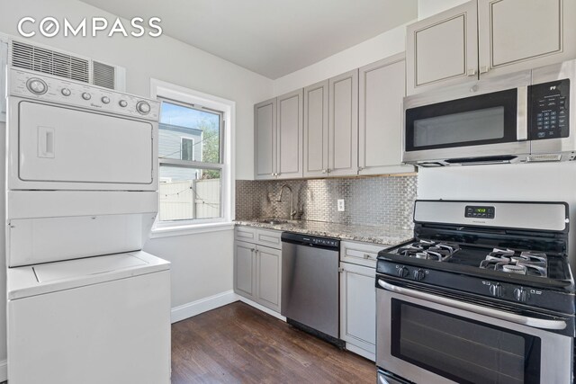 269 Ainslie St, New York City, NY 11211 - kitchen with decorative backsplash, stacked washer / dryer, appliances with stainless steel finishes, dark wood finished floors, and baseboards