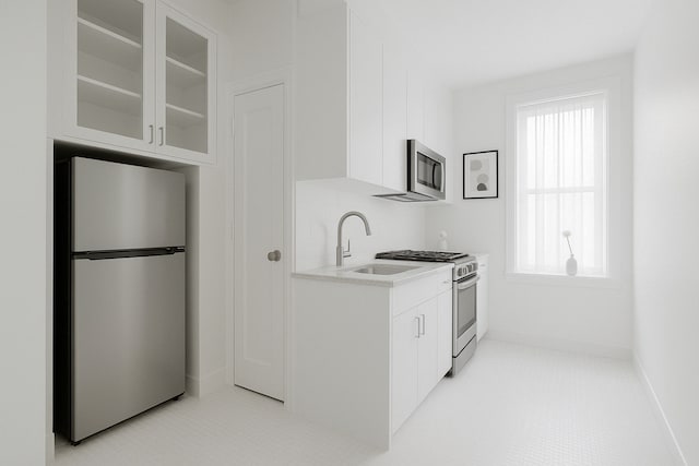 kitchen with stainless steel appliances, white cabinets, glass insert cabinets, a sink, and light countertops