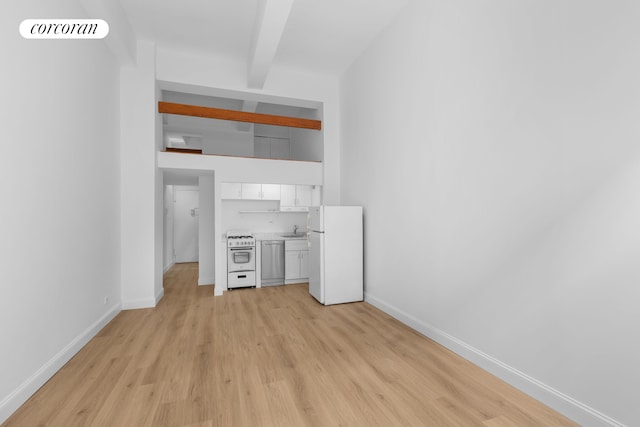 unfurnished living room featuring a sink, light wood-style flooring, beam ceiling, and baseboards