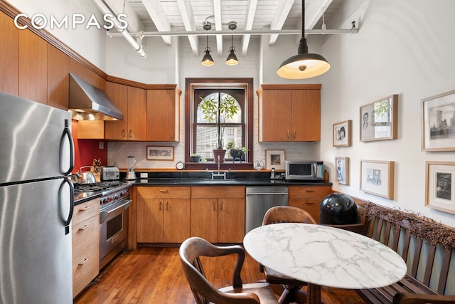 210 Spring St Unit 5, New York City, NY 10012 - kitchen with dark countertops, appliances with stainless steel finishes, light wood finished floors, wall chimney exhaust hood, and beamed ceiling