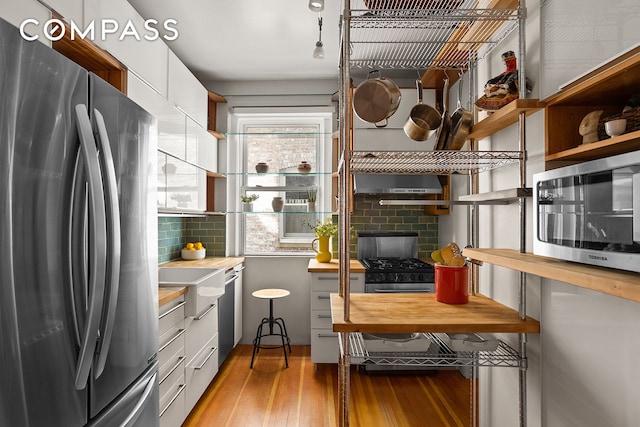 kitchen with open shelves, white cabinets, stainless steel appliances, light wood-type flooring, and backsplash