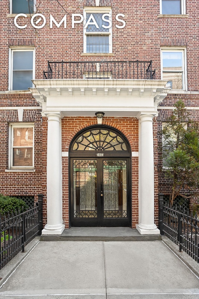 view of exterior entry with a balcony, french doors, and brick siding