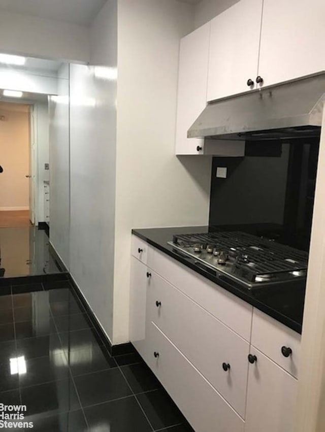 15 W 53rd St Unit 27E, New York City, NY 10019 - kitchen featuring under cabinet range hood, white cabinetry, stainless steel gas cooktop, dark countertops, and baseboards