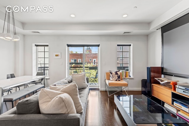living room with wood finished floors, recessed lighting, a tray ceiling, and baseboards