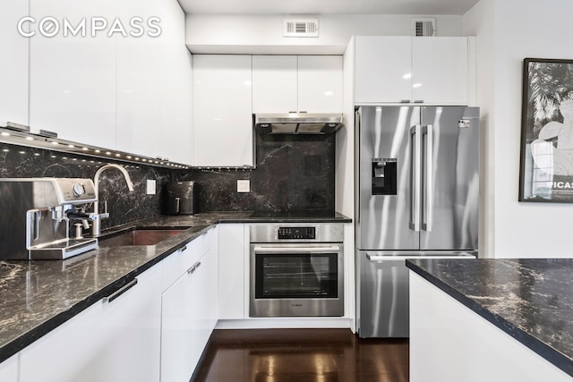 kitchen featuring stainless steel appliances, a sink, white cabinets, under cabinet range hood, and backsplash