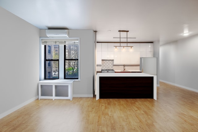 kitchen with modern cabinets, light countertops, a wall mounted air conditioner, white cabinets, and light wood finished floors