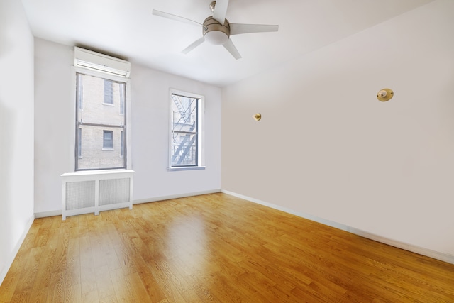 unfurnished room featuring radiator heating unit, light wood-style flooring, a ceiling fan, baseboards, and a wall mounted air conditioner