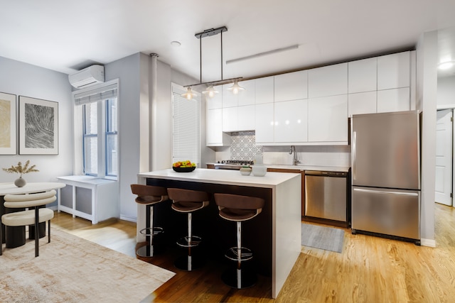kitchen featuring appliances with stainless steel finishes, a wall unit AC, light wood-style flooring, light countertops, and white cabinets