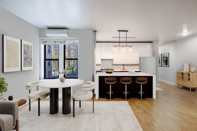 dining space with a wall mounted air conditioner, light wood-style floors, and baseboards