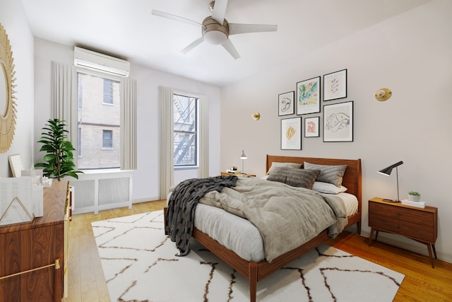 bedroom with light wood-style flooring, a wall unit AC, radiator, and ceiling fan